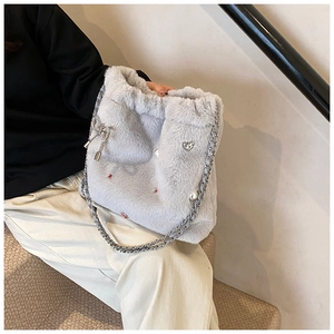 Gros plan sur un cabas en peluche gris clair avec charms en perles et détails cœur argentés