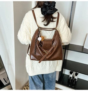 Detail of dark brown leather tote bag with baseball pendant and knit texture