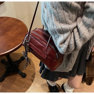 Detail of vintage burgundy PU leather shoulder bag with chocolate charm and dual zippers