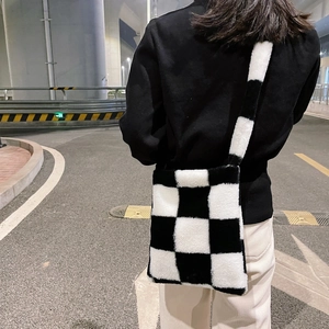 Detail view of black and white checkerboard plush crossbody bag on a person's shoulder
