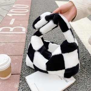 Close-up of soft black and white checkered plush tote bag held by a model outdoors