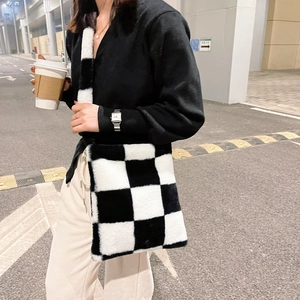 Close-up of black and white checkered plush shoulder bag with wide strap on a model