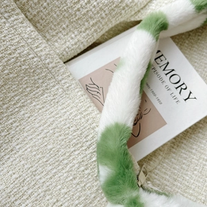 Detailed close-up of cream tweed fabric and soft plush green handle on a fashion handbag