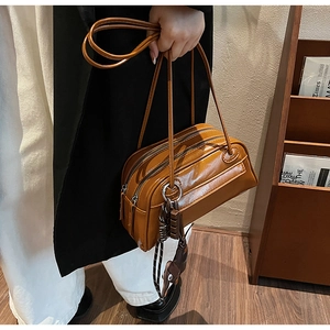 Detail view of a vintage brown PU leather shoulder bag with double zipper and woven charm