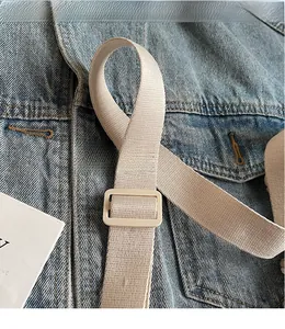 Detail of adjustable beige nylon shoulder strap with smooth plastic buckle on denim