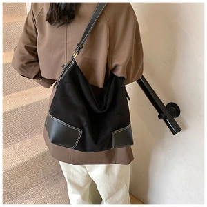 Detail of contrast stitching and adjustable leather strap on a black suede tote bag