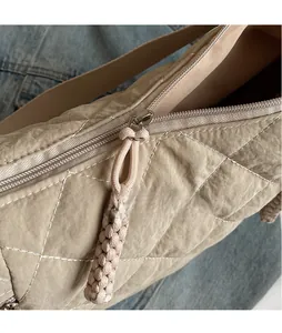 Close-up of silver metal zipper with beige woven puller on quilted dumpling shoulder bag