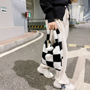 Detail of soft black and white checkerboard plush tote bag held by hand outdoors