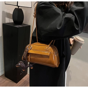 Detail of caramel PU shoulder bag with dachshund charm on black coat background