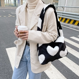 Détail d'un sac d'épaule en peluche noir à motifs de cœurs blancs dans un décor urbain