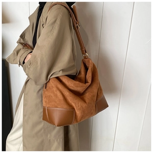Detail of a large brown suede hobo bag featuring contrast stitching and a long strap