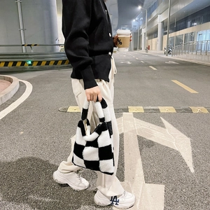 Close-up of black and white checkerboard plush handbag carried during a street walk