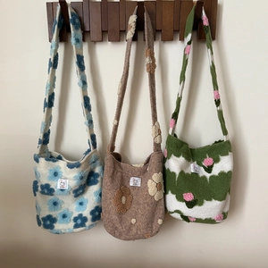 Three plush shoulder bags with floral patterns on wooden hooks against a white wall
