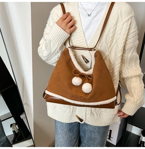 Detail of brown suede tote bag with white faux fur trim and dual fur ball bow decor