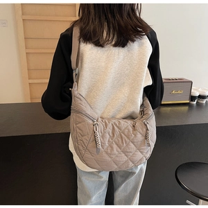 Detail of grey quilted crescent shoulder bag featuring premium stitching and woven zipper puller