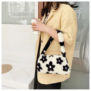 White plush underarm bag with black floral pattern shown on shoulder by a model