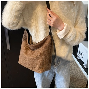 Detailed view of brown plush bucket bag with leather strap on a model wearing a white sweater