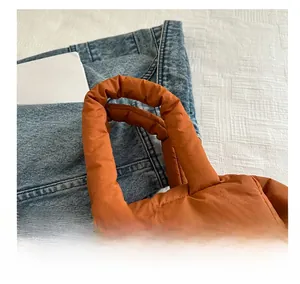 Detailed close-up of soft quilted orange puffy handbag handles and stitch texture