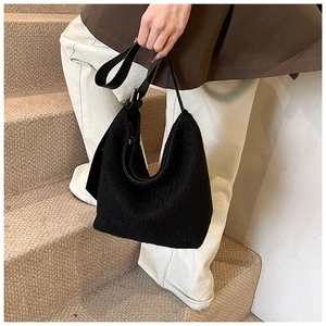 Close-up of black plush fabric texture and adjustable leather strap on a shoulder bag