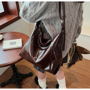 Détail d'un grand sac cabas en cuir verni marron foncé dans un café moderne chic