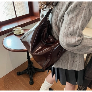 Détail d'un grand sac hobo en cuir PU marron foncé poli porté à l'épaule pour femme