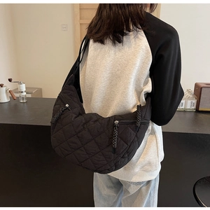 Detail of black quilted crescent bag showing textured nylon fabric and woven zipper pull