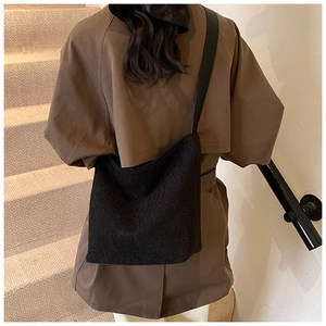 Detail of minimalist black textured wool shoulder bag worn with a brown trench coat