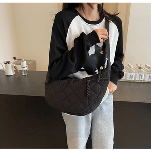 Detail of black quilted crescent crossbody bag featuring texture and woven zipper pull