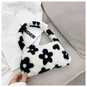 Detail of soft white faux fur handbag with black floral pattern on a grey sofa