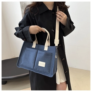 Detail of blue canvas tote bag with front pockets and adjustable strap on a model