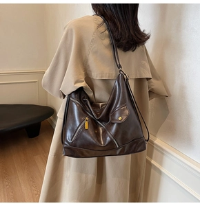 Detail of a large brown PU leather tote bag with biker-style zippers shown on a model