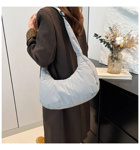 Détail du sac croissant en nylon matelassé bleu clair porté à l'épaule par le mannequin