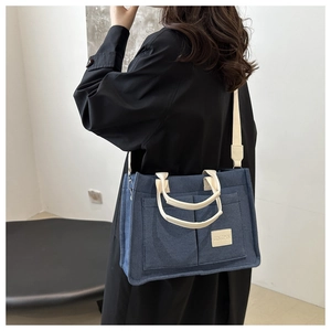Blue canvas tote bag with dual front pockets and cream white straps worn by a model