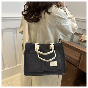 Detail of a minimalist black canvas tote bag with front pockets and white brand label