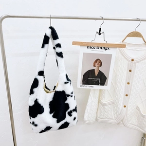 Detail of plush faux fur tote bag with cow print pattern hanging on a metal hanger