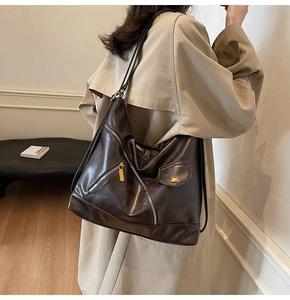 Detail of dark brown faux leather tote bag with functional zippers on a beige trench coat