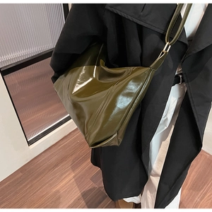 Détail du sac hobo vert foncé brillant avec large bandoulière porté sur un manteau noir