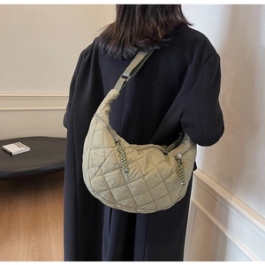 Detail of light olive green quilted half-moon bag with large diamond stitching and woven zipper