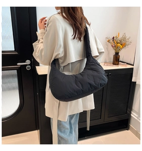 Close-up of a soft quilted black crescent shoulder bag worn by a model in a modern room