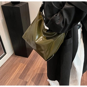 Sac hobo en cuir verni vert foncé brillant porté avec un trench-coat d'automne minimaliste chic