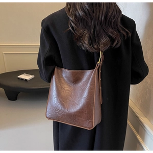 Detail view of deep brown vintage leather tote bag worn as a shoulder bag by a model