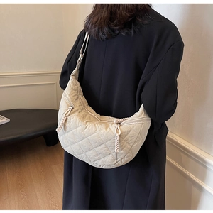 Detailed view of beige quilted dumpling bag with wide shoulder strap worn over black coat