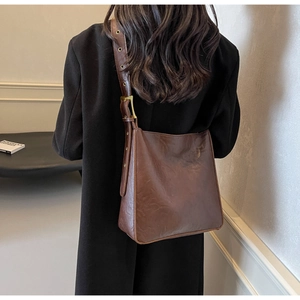 Detail view of brown vintage leather shoulder bag with metallic eyelet strap on a black coat