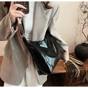 Détail d'un cabas en cuir verni noir brillant avec logo de la marque embossé sur le côté