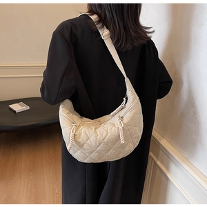 Rear view of a beige quilted hobo bag with adjustable wide strap on a dark coat