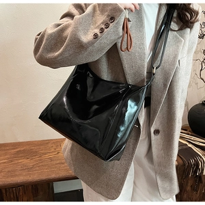 Sac à bandoulière chic en cuir verni noir avec finition brillante porté par un mannequin