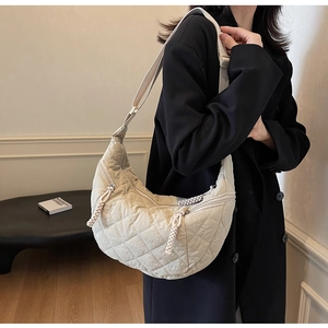 Detail view of quilted cream dumpling bag with adjustable strap and woven zipper puller