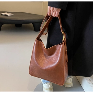 Macro view of vintage brown leather tote bag showing glossy texture and gold buckle detail
