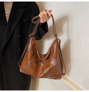 Detail of vintage brown PU leather shoulder bag featuring asymmetric zipper and buckle pocket