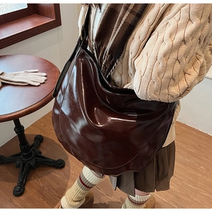 Detail of a large dark brown patent leather hobo bag worn by a model in a cozy indoor setting